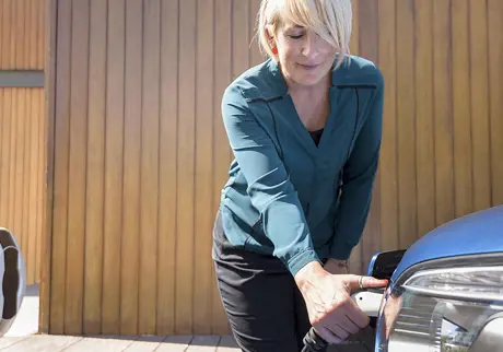 Kvinna laddar elbil på garageuppfart